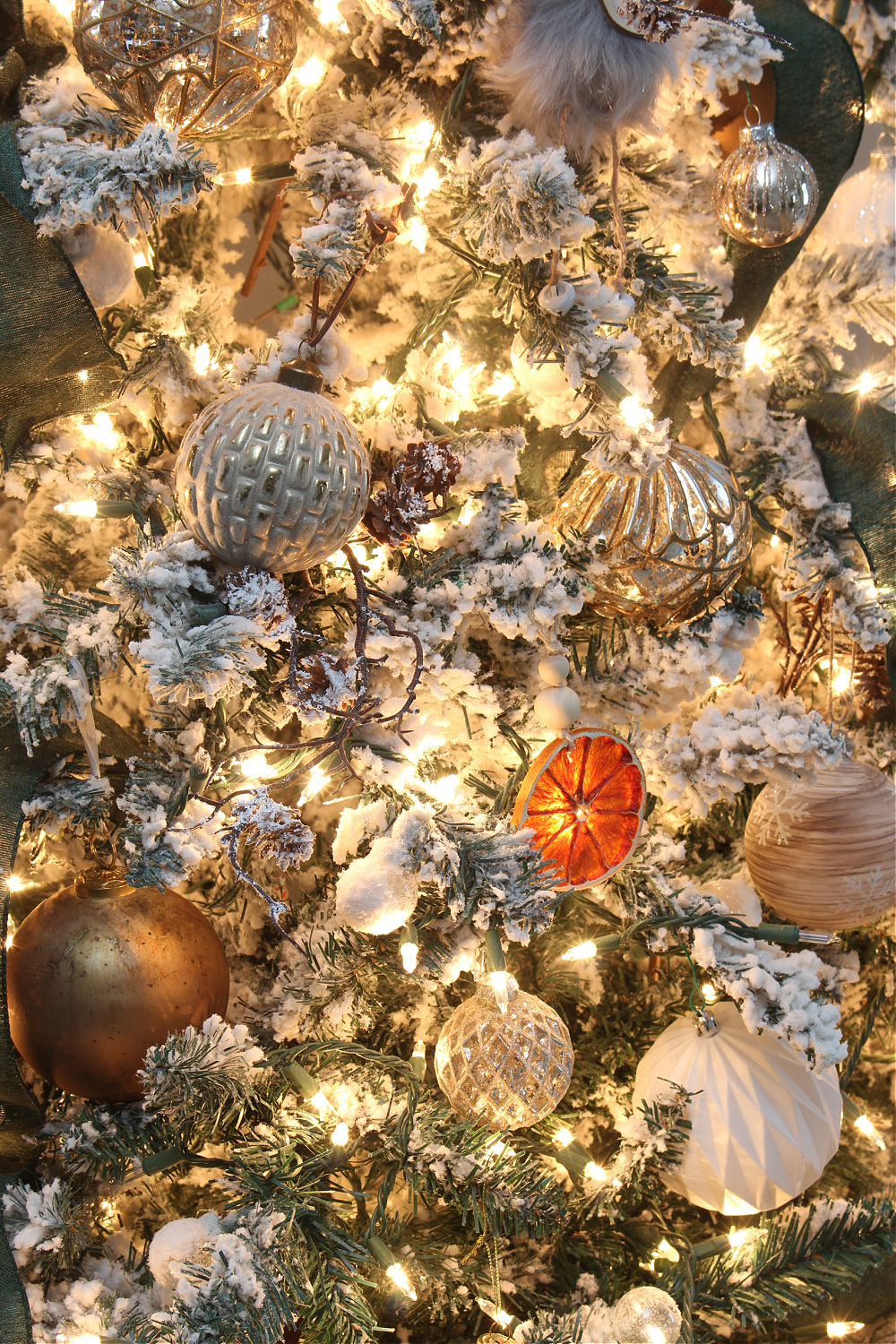 Metallic Christmas tree ornaments and dry orange ornaments are illuminated by Christmas lights.
