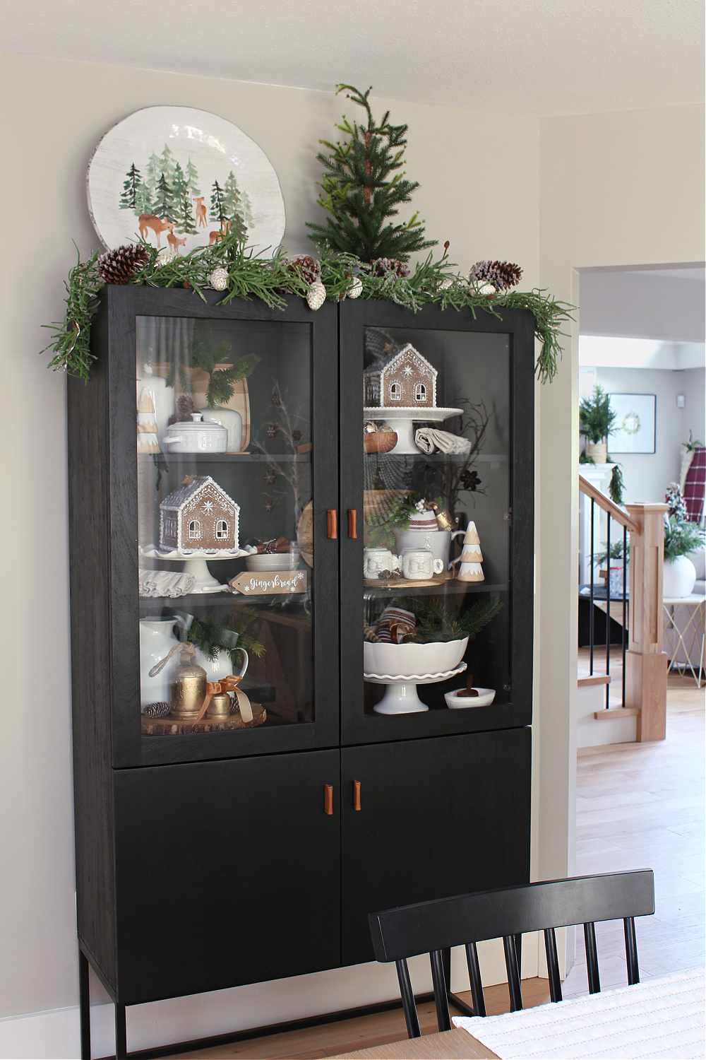 Black cabinet decorated for Christmas with gingerbread houses, greenery, and white dinnerware.
